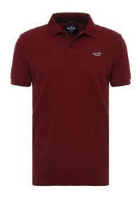 Mörkröd polo-shirt i mjukt tyg, med krage, tre-knapp placket och en liten logotyp på bröstet. Korta ärmar.
