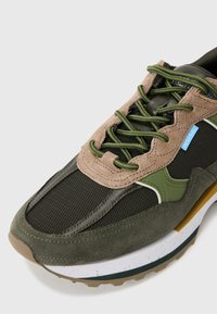 Läbivõrguga tenniseketsid, mis on valmistatud mustast võrgust, oliivrohelisest sametist ja beežite detailidega. Tekstuuriga tald, millel on valged ja rohelised aktsendid.