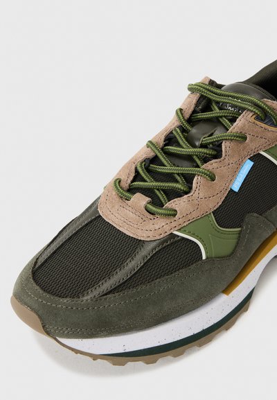 Adidași cu șireturi, realizati dintr-un amestec de plasă neagră, suede verde măsliniu și accente bej. Tălpi texturate cu detalii albe și verzi.
