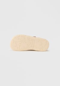 Σόλα υποδήματος με υφή, από ελαφρώς λευκό καουτσούκ. Διαθέτει σχεδιασμό πέλματος με μοτίβο σε διάφορα σχήματα και το όνομα της μάρκας εμφανώς ανάγλυφο.