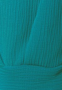 Tissu texturé bleu sarcelle avec nervures verticales, détail de taille froncée. Matière douce et légère avec une apparence fluide.