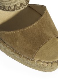 Espadrille en suède marron avec un bout ouvert, présentant un dessus en tissu tissé et une semelle en jute, cousue avec un fil beige.