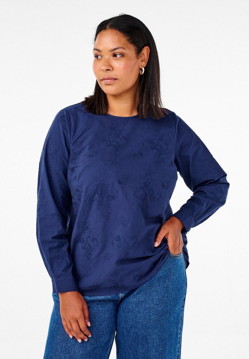 Marinblå långärmad skjorta med en subtil blommig struktur, rund halsringning och avslappnad passform. Tillsammans med blåjeans, vilket ger en avslappnad look.