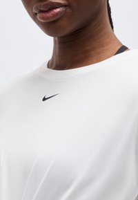 Κοντινή λήψη ενός ατόμου που φοράει άσπρο πουκάμισο Nike με μαύρο λογότυπο σβούρας κοντά στον γιακά.