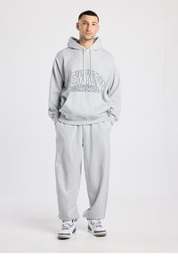 Grijze hoodie met "NEW YORK SPORTSWEAR" in zwart gedrukt, gecombineerd met bijpassende grijze joggingbroek en witte sneakers. Casual, comfortabele pasvorm.