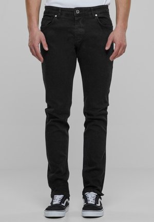 Mustat farkut, jotka ovat slim fit -mallia, viisi taskua ja kontrastiväriset saumat, yhdistettynä mustiin ja valkoisiin lenkkareihin.