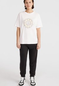 Vit oversized t-shirt med ett färgglatt tryck, kombinerad med svarta sweatpants och svarta och vita mönstrade sneakers. Avslappnad och bekväm passform.