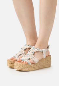 Platform sandals with woven tan and light blue macramé upper, featuring a strap and ankle buckle, and a textured cork wedge sole.