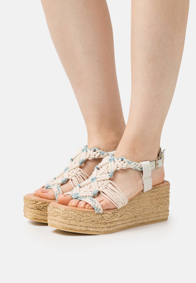 Platform sandals with woven tan and light blue macramé upper, featuring a strap and ankle buckle, and a textured cork wedge sole.