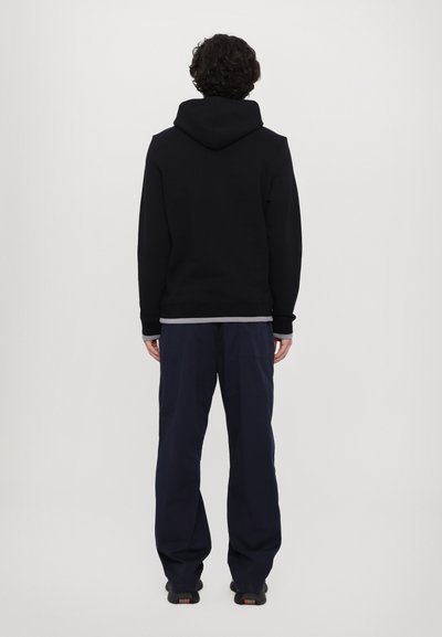 Black hooded sweatshirt with a soft texture, paired with loose-fitting navy blue trousers and black shoes. Visible seams and cuffs.