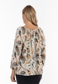 Blusa leggera con un motivo floreale paisley in arancione, verde e nero su uno sfondo crema, con scollatura arricciata e maniche lunghe.