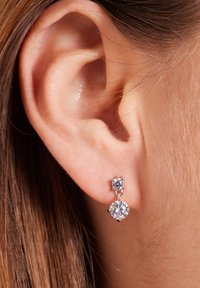 Silberne Tropfenohrringe mit zwei klaren Kristallen, einem quadratischen oben und einem runden unten, mit glänzender Oberfläche und klassischem Design.