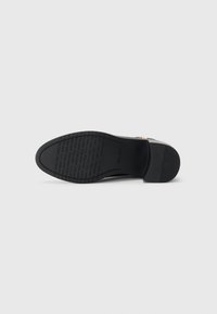Black leather shoe sole with a textured surface, featuring a slight heel and embossed brand name. Flat, smooth edges with minimal detail.