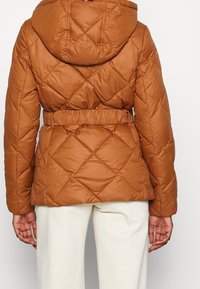 Giacca a vento marrone trapuntata con cappuccio e vita elasticizzata. Presenta un motivo a rombi e un design con cintura. Tessuto morbido, materiale caldo.