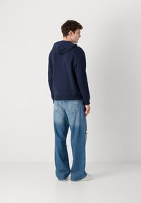 Felpa blu navy con cappuccio regolabile, abbinata a jeans a gamba larga chiari e strappati. Presenta polsini e orlo a costine.