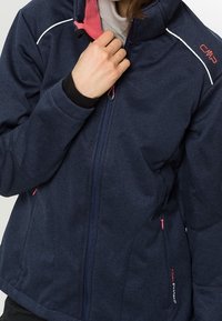Chaqueta de forro polar azul marino con un cuello alto, acentos interiores en rosa, detalles de costura blanca y bolsillos laterales con cremallera. Presenta la marca CMP.