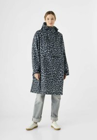 Jas met luipaardmotief in zwart en lichtblauw, met een hoge kraag en lange mouwen. Gecombineerd met opgerolde grijze jeans en witte sneakers.