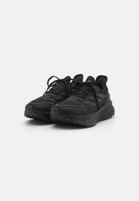Chaussures de sport noires avec un dessus texturé, un orteil renforcé et une semelle en caoutchouc. Présente un logo proéminent et un système de laçage pour un ajustement sécurisé.