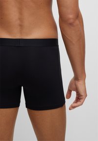 Schwarze Baumwoll-Boxershorts mit einfachem Design. Glatte Textur, elastischer Bund und minimalistische Nähdetails. Rückansicht des Oberkörpers.