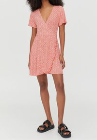 Robe portefeuille rouge à fleurs avec des manches courtes, décolleté en V profond, ourlet volanté et tissu léger, assortie à des sandales à plateforme noires.