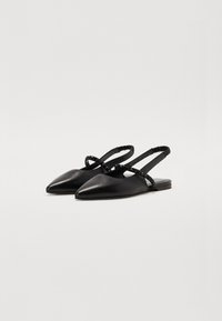 Chaussures noires en cuir à bride arrière avec des pointes, présentant des sangles texturées avec de petites accents. Semelle plate et finition lisse.