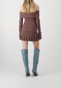 Hnědé mini šaty bez ramínek s žebrovanou texturou a skládáním na sukni. V kombinaci se světle modrými, po kolena sahajícími, stiletto botami na vysokém podpatku.