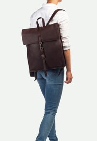 Mochila de cuero marrón con diseño de solapa, correas ajustables y un acabado sutilmente texturizado. Presenta un cierre de clip y líneas elegantes.