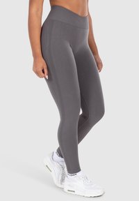 Hoch taillierte, graue Leggings mit strukturierten Akzenten und glatter Oberfläche, kombiniert mit weißen Sportschuhen.