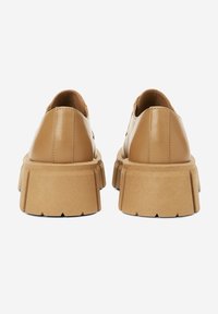 Chaussures en cuir marron avec une semelle épaisse et texturée. Présente un dos arrondi et des détails sur les côtés, conçues pour le confort et la stabilité.