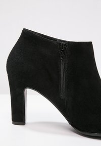 Bottine en daim noir avec un talon bloc haut. Dotée d'une fermeture éclair latérale et d'une texture lisse, avec une silhouette élégante et structurée.