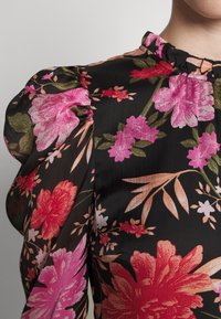 Květinová blůza s nabíranými rukávy, černé pozadí, s velkými růžovými a oranžovými květy, zelenými listy a volánkovým výstřihem.