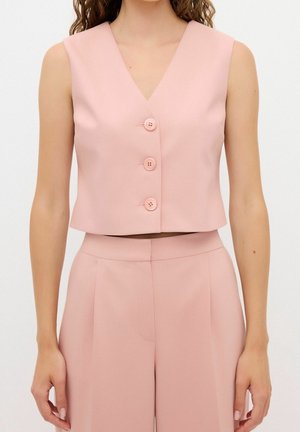 Mujer con chaleco corto sin mangas rosa con tres botones, combinado con pantalones rosa de pierna ancha y cintura alta.