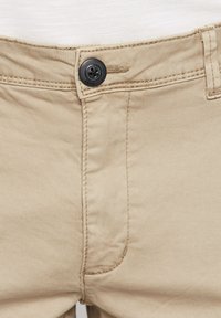 Khaki trousers with a zip fly and button closure, featuring a front pocket, subtle stitching details, and smooth cotton fabric texture.