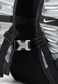 Sac à dos Nike en tissu noir, avec des bretelles texturées, une boucle argentée en accent, et un panneau flexible à l'arrière pour le soutien.