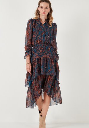 Flowy, tiered dress in dark teal with orange floral paisley patterns. Features long sleeves, a smocked waist, and sheer fabric texture.