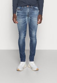Pantalones vaqueros skinny azul de denim con un acabado desgastado, que cuentan con cinco bolsillos y un botón de cobre; combinados con zapatillas blancas.