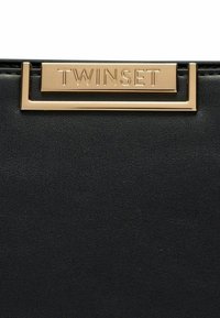 Sort tekstureret læderhåndtaske med en guldfarvet metalplade indgraveret med "TWINSET," som fremhæver et slankt og moderne design.