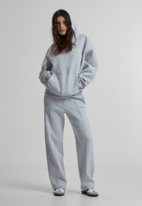Grauer Kapuzenpullover mit Fronttasche, kombiniert mit passenden grauen Jogginghosen mit kontrastierenden Nähten. Lässiger, entspannter Schnitt.