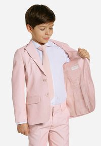 Traje rosa claro con chaqueta de dos botones, bolsillos de solapa, corbata a juego y camisa blanca, que destaca por su textura suave y un ajuste a medida.