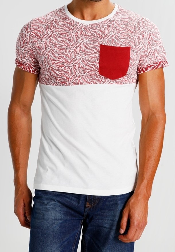 Homme portant un T-shirt blanc et rouge à manches courtes avec un motif de feuilles sur la moitié supérieure et la moitié inférieure unie, associé à un jean bleu.