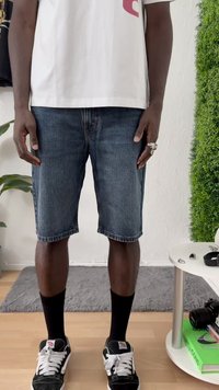 Šorti no auduma, tumši zili, līdz ceļgaliem, ar taisnu griezumu. Apvienoti ar baltu grafisku t-kreklu un melniem sporta apaviem ar baltiem šņorēm.