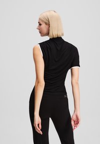 Melna bezpiedurkņu blūze ar augstu apkakli un baltu apdari. Gluda struktūra un pieguļoša dizaina. Saskaņota ar melnām biksēm ar diskrētām kabatām.