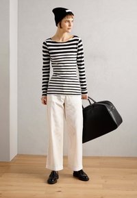 Svart och vit randig långärmad topp, vita vida byxor, svarta loafers och en stor svart läderväska, bärs med en svart mössa.