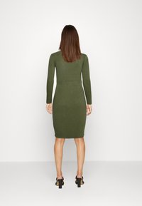 Robe en tricot de couleur vert foncé, avec des manches longues, une taille cintrée et une longueur jusqu'au genou. Présente une texture côtelée et des détails de galbe subtils.