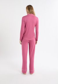 Różowa, długorękawowa piżama z kołnierzem i białym wykończeniem, w komplecie z pasującymi różowymi spodniami ozdobionymi kontrastującymi białymi akcentami na mankietach.