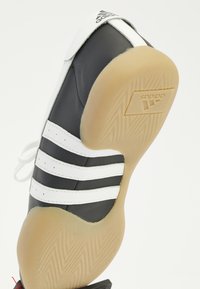 Svart och vit Adidas-sneaker med gummisula, tre vita ränder på sidan och Adidas-logotyp på häl och sula.