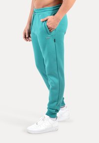 Spodnie dresowe w kolorze morskim o swobodnym kroju, z bocznymi kieszeniami i elastycznymi mankietami. Noszone z białymi trampkami. Miękki bawełniany materiał.