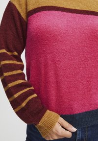 Pull multicolore avec un dégradé de rose, marron et or. Texture douce avec des manches rayées et des poignets côtelés, ourlets en bleu foncé.