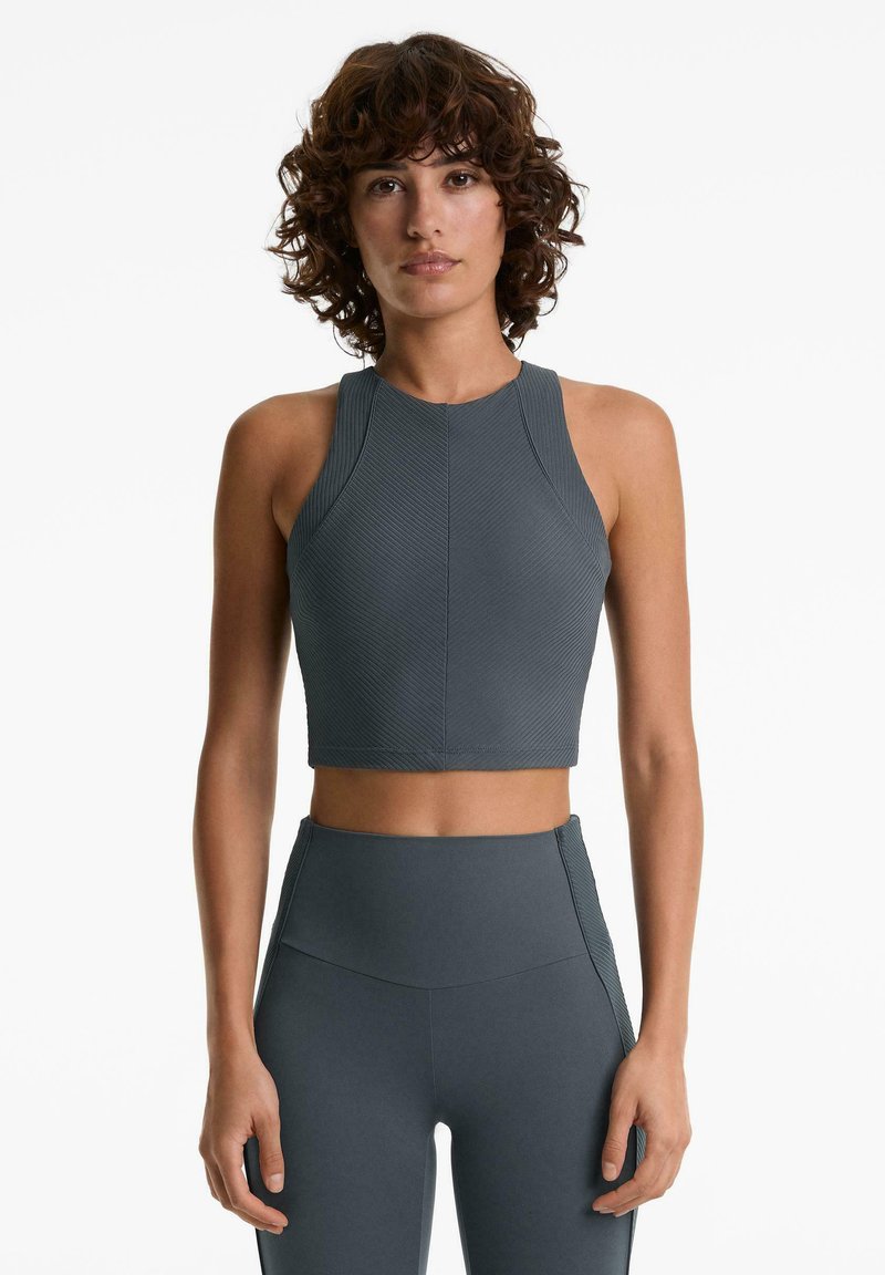 Haut de sport court gris foncé avec texture côtelée, col montant et larges bretelles. Associé à un legging taille haute assorti.