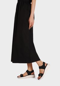 Sandali neri con una fascia testurizzata e fibbie, abbinati a una lunga gonna nera. I sandali presentano una suola a zeppa bianca per un maggiore slancio.